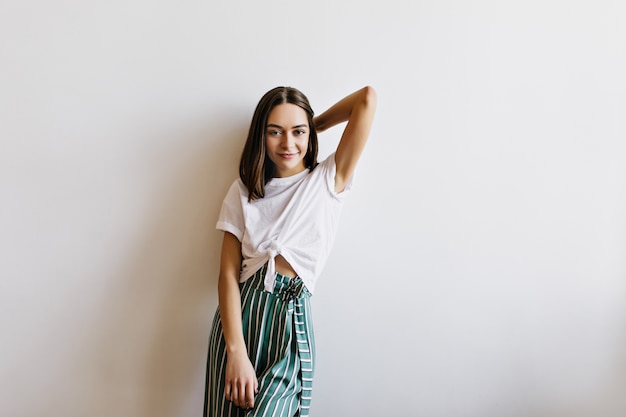 Interested girl with straight hairstyle posing at home in weekend morning. stylish caucasian woman wears green pants.