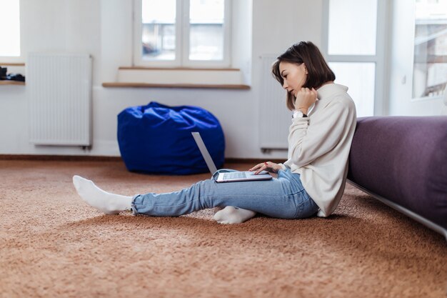 Interested student woman works on laptop computer sitting on the floor at home in day time casual dressed