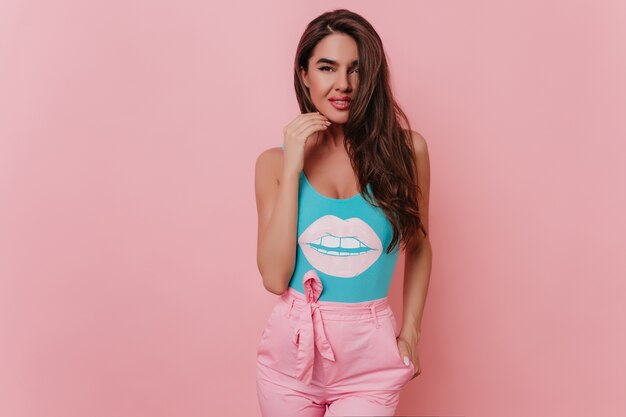 Interested tanned woman in colorful summer outfit standing on pink space