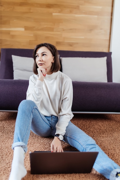 Interested woman works on laptop computer sitting on the floor at home in day time casual dressed