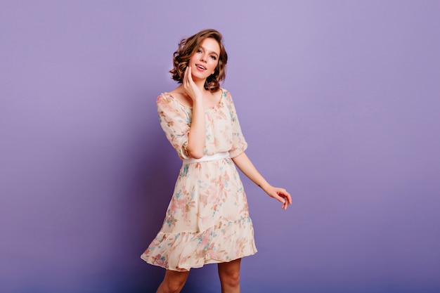 Interested young woman in cute dress gently touching her face on purple background