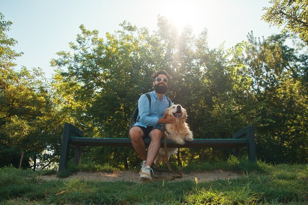 公園の椅子に彼の犬と一緒に座っている面白い男