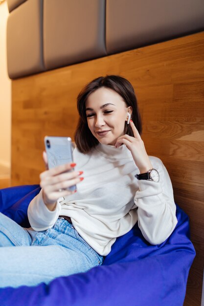 재미있는 여자는 그녀의 친구와 문자 메시지에 대한 그녀의 전화를 사용하여 밝은 보라색 가방 의자에 앉아있다