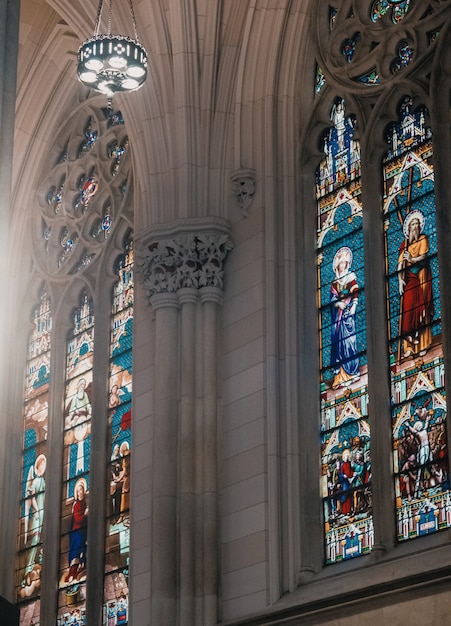 The interior of a church with gray walls and mosaic paintings of religious saints on windows