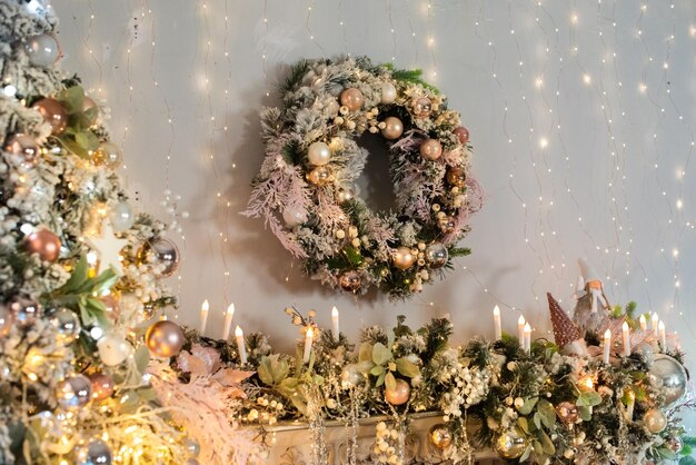 Интерьер в розовых и золотых тонах. елка, венок украшены блестящими шарами, огоньками, свечами. с новым годом
