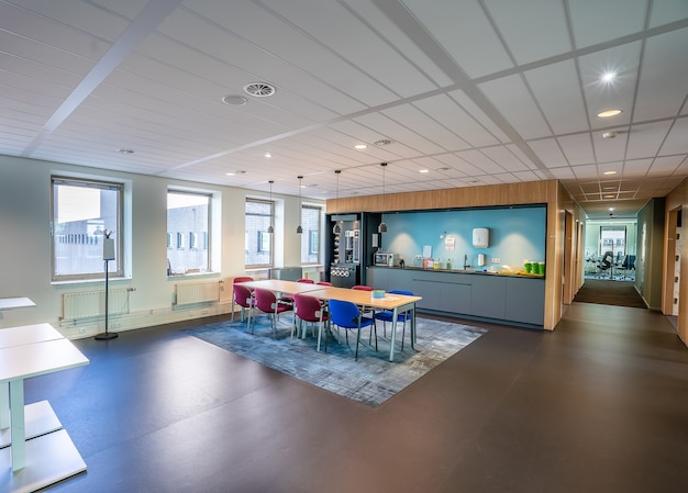 Interior of the kitchen area of a modern office with a long wooden table and chairs