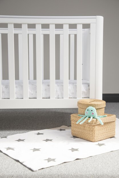 부드러운 별이 빛나는 카펫에 현대적인 아늑한 유아용 침대와 짠 고리 버들 세공 상자가 있는 가벼운 아기 방의 내부