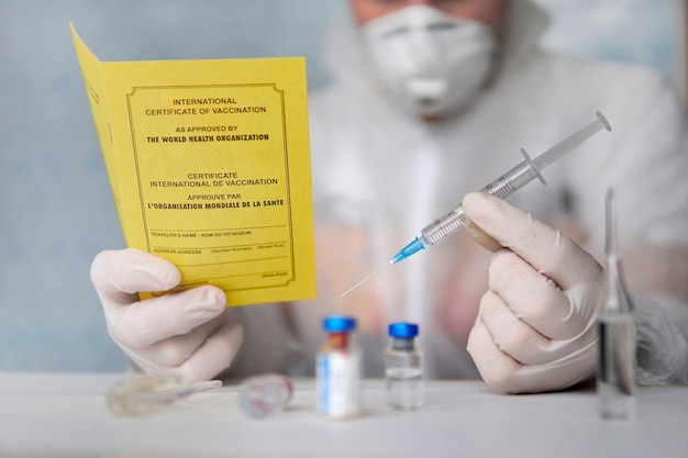 作成されたワクチンを記録するための文書である国際ワクチン接種証明書。ドキュメントは黄色です。外国人のパスポートとテーブルの上の注射器。安全な旅行の概念。