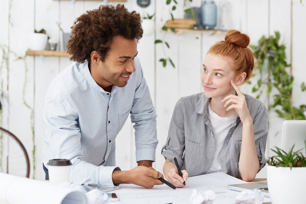 International united team of two creative coworkers sitting at desk with blueprints