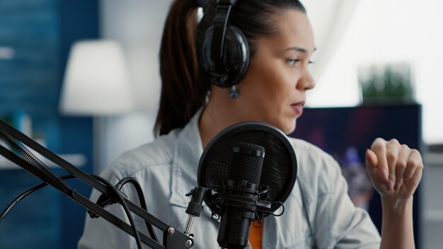 Internet live radio talk show host with headphones talking to audience at microphone in studio. Creative content creator sitting at desk while hosting podcast broadcast in living room.