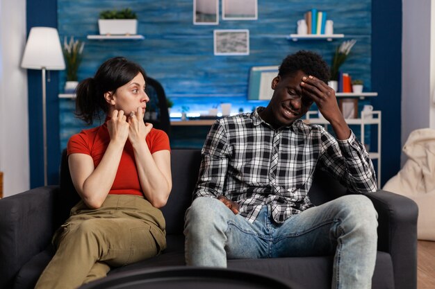 Interracial couple getting into argument sitting on couch