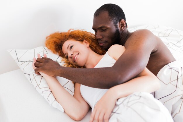 Interracial couple holding hands in bed