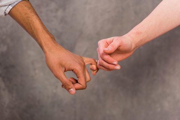 Interracial couple's hand holding each other's finger against concrete backdrop