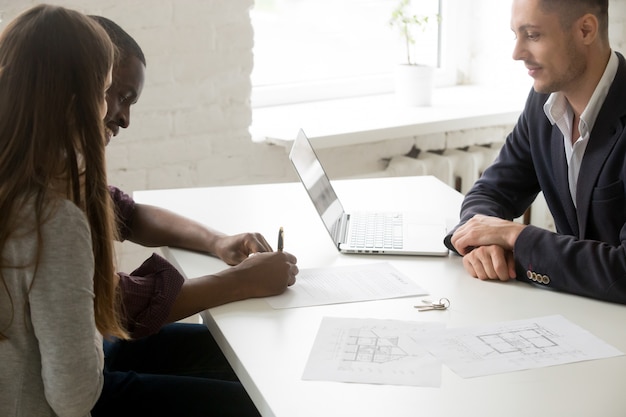 Interracial couple signing mortgage investment contract at meeting with broker 