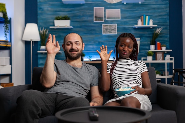 Interracial couple waving at video call camera using technology