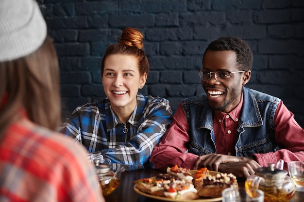Interracial group of three friends dining at restaurant, spending good time together