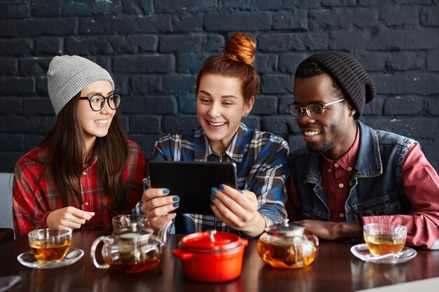 Interracial group of three hipsters using touch pad at cafe