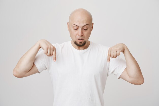 Intrigued bald adult bearded man pointing down, look curious