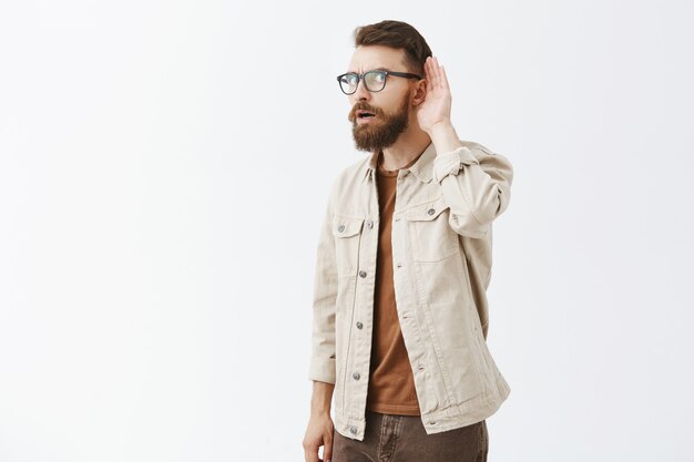 Intrigued bearded man in glasses posing against the white wall