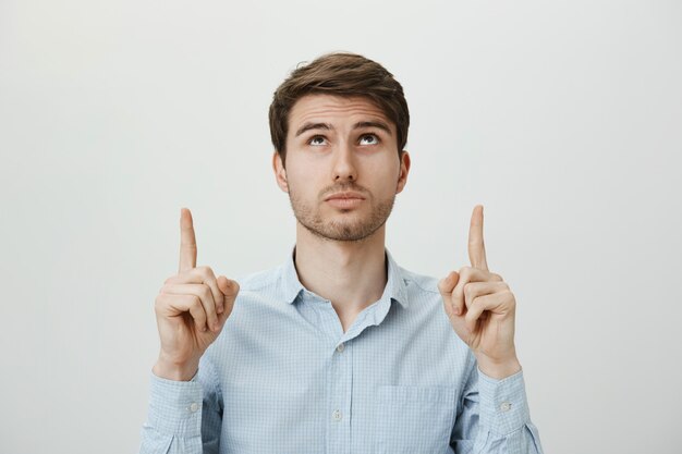 Intrigued bearded young man looking and pointing up at advertisement