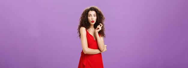 無料写真 赤いドレスに巻き毛のヘアスタイルと不思議なことに唇を折り畳む口紅を持つ興味をそそられた chaming エレガントな女性