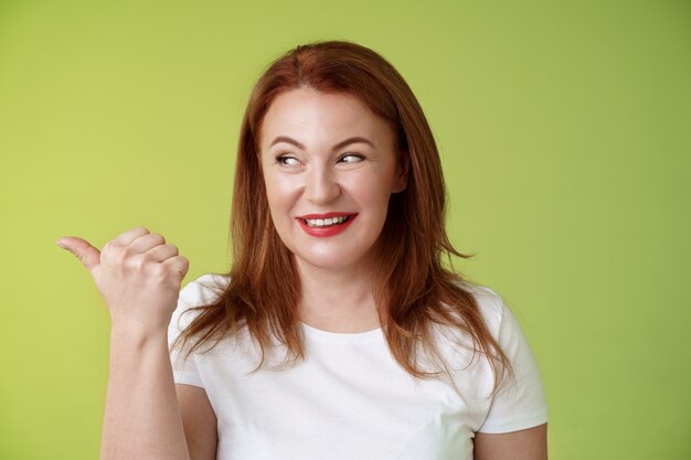 Intrigued charismatic redhead middleaged woman smiling temtation interest pointing looking left curiously