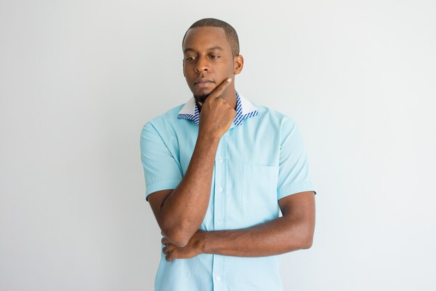 Introspective handsome young African man rubbing chin and looking down. 