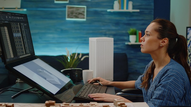 Invalid architect using touch screen for building layout in engineering office. Woman engineer sitting in wheelchair working on blueprint plan with technology for construction project