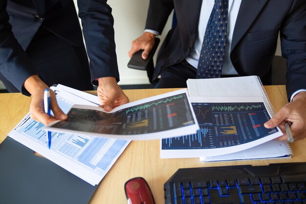 Free photo investor and trader discussing statistic data, holding papers with financial charts and pen. cropped shot. broker job or trading concept