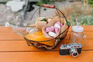 Free photo iron basket with bottle of orange juice and sandwiches standing on wooden table. outdoor photo of meal for picnic, empty glass and camera.