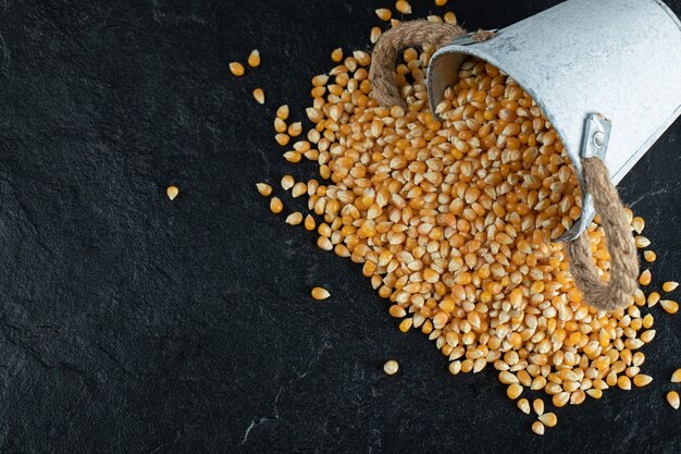 An iron bucket with uncooked corn grains on dark surface