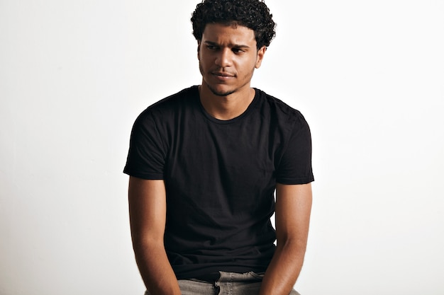 Free photo ironic thoughtful handsome young man with an afro wearing a black sleeveless cotton t-shirt on white wall