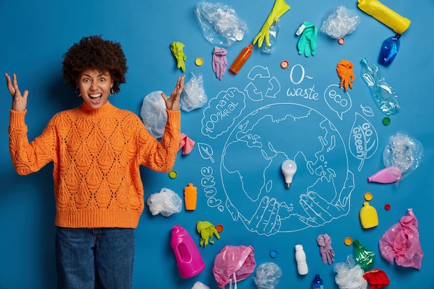 Free photo irritated curly haired woman raises both hands with anger, concerned with big environmental problem, gestures against plastic waste, annoyed by polluters.