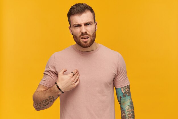 Free Photo | Irritated handsome young man in pink tshirt with beard and tattoo on hand points at himself by hand and looks annoyed over yellow wall Free Photo | Irritated handsome young man in pink tshirt with beard and tattoo on hand points at himself by hand and looks annoyed over yellow wall