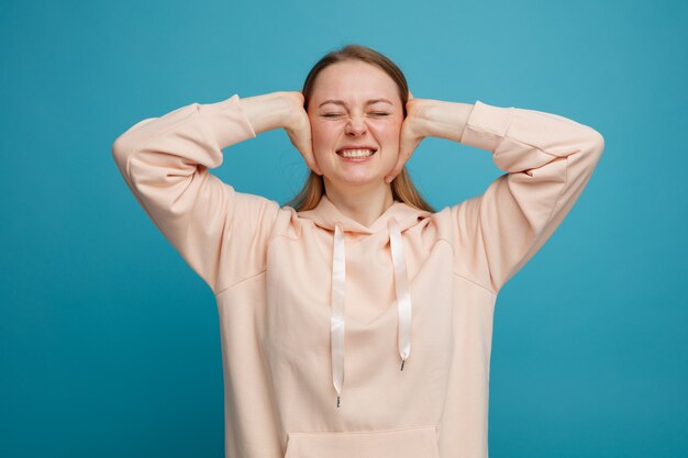 目を閉じて手で耳を覆うイライラした若いブロンドの女性