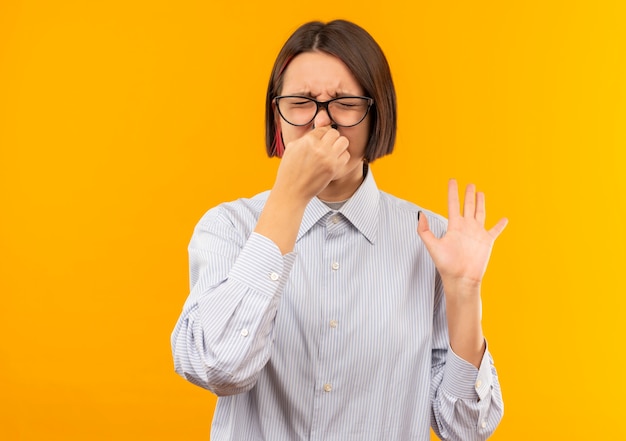 Foto gratuita giovane ragazza irritata della call center con gli occhiali che tiene il naso e che mostra la mano vuota con gli occhi chiusi isolati sull'arancio