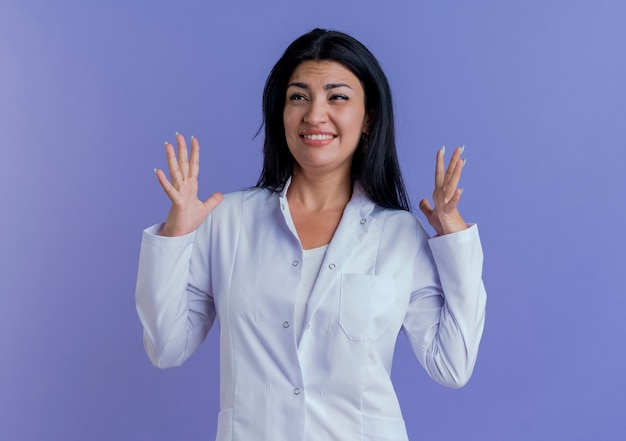 Irritated young female doctor wearing medical robe keeping hands in air looking at side 