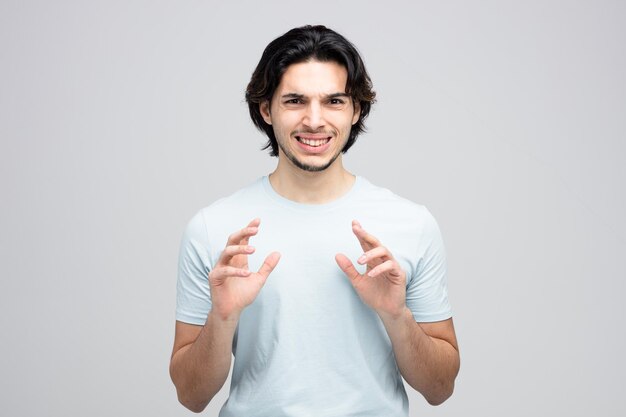 Irritated young handsome man keeping hands in air while looking at camera isolated on white background