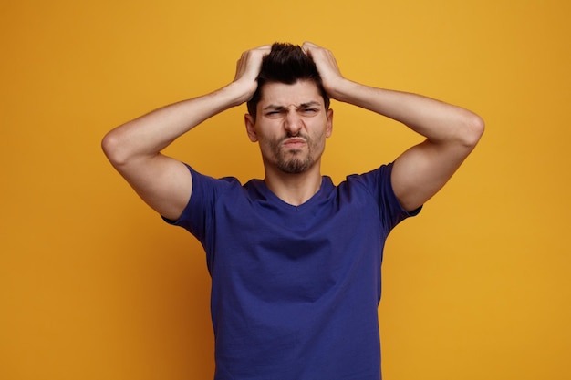 Free photo irritated young handsome man keeping hands on head looking at camera on yellow background