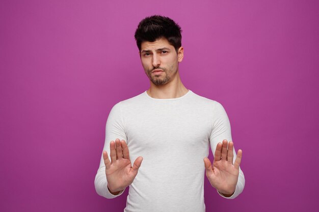 Irritated young handsome man looking at camera doing no gesture on purple background