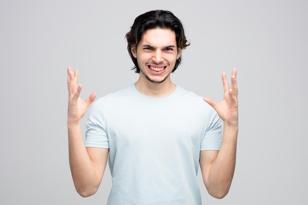 irritated young handsome man looking at camera keeping hands in air isolated on white background