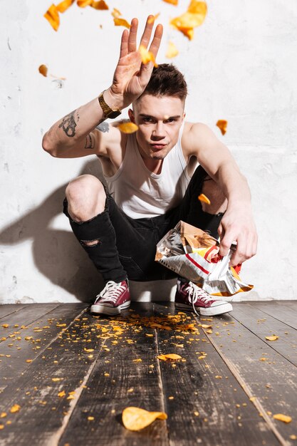Irritated young man throwing potato chips out from packet
