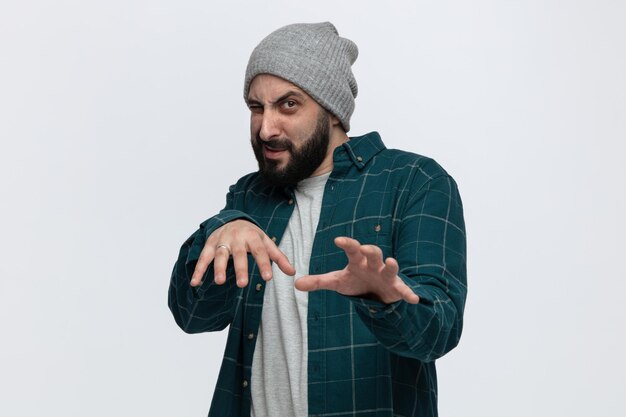 Free photo irritated young man wearing winter hat looking at camera stretching hands out towards camera doing no gesture isolated on white background