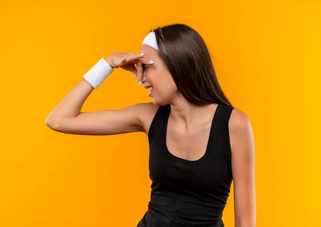 Irritated young pretty sporty girl wearing headband and wristband holding nose isolated on orange wall