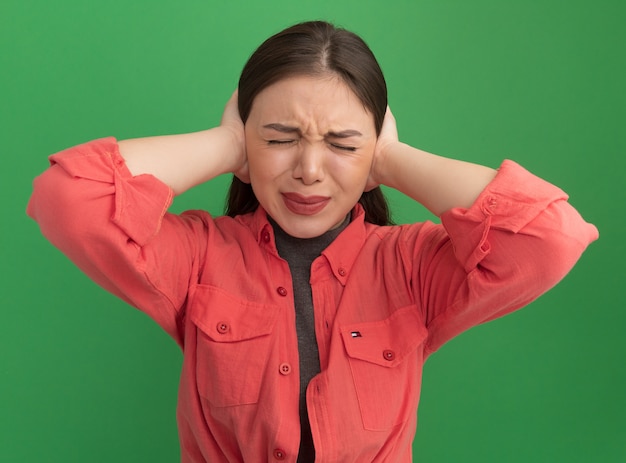 Free photo irritated young pretty woman covering ears with hands with closed eyes isolated on green wall