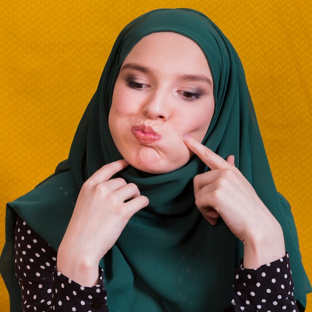 Free photo islamic woman making funny face against yellow backdrop