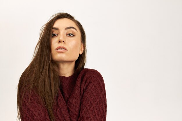 Isolated image of good looking beautiful young woman with long borwn hair warming up in knitted sweater posing against white studio wall background with copy space