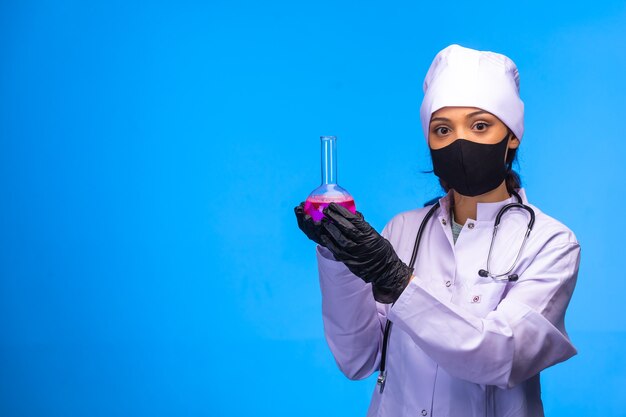 Isolated nurse in hand and face mask holds chemical flask on blue background. 