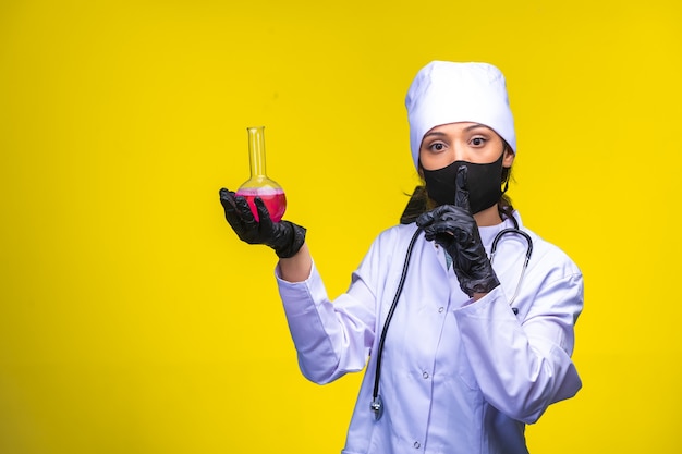 Isolated nurse in hand and face mask holds chemical flask and makes point to danger