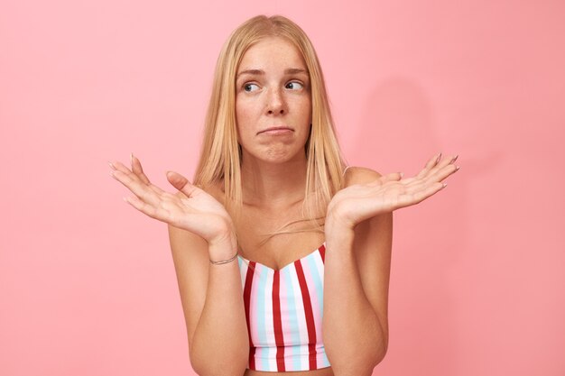 Isolated Portrait of confused perplexed beautiful young Caucasian woman making helpless gesture, having uncertain doubtful facial expression